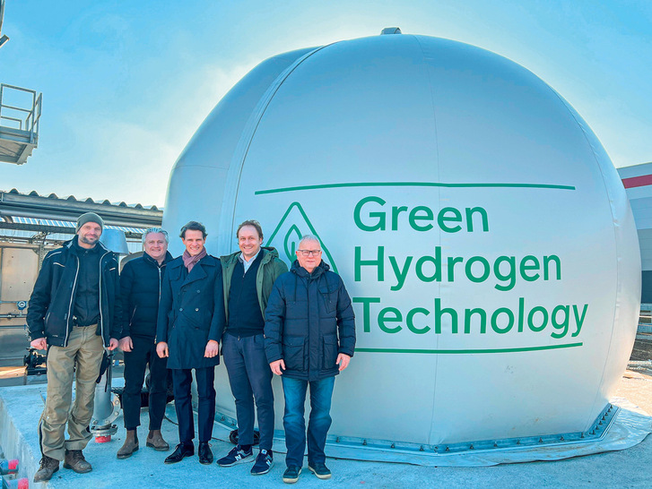 „Fünf Fachleute der Kälte- und Klimatechnik stehen vor einem großen Gebäude mit der Aufschrift ‚Kälteinnovationen und Energiemanagement‘ unter klarem, blauen Himmel. - © Bild: Westfalen AG