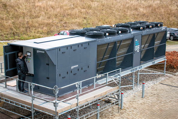 Gerne! Ein optimierter Alt-Text für das genannte Bild könnte wie folgt aussehen:
„Techniker bei der Wartung einer großen, industriellen Kälteanlage auf einer erhöhten Plattform im Freien. Fokus auf energieeffiziente Steuerungstechnik und Nachhaltigkeit. - © Bild: Advansor