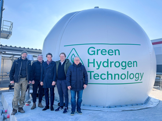 Alternativer Alt-Text: „Fünf Fachleute für Kältetechnik diskutieren innovative Lösungen für die Integration von grüner Wasserstofftechnologie in kälte- und klimatechnische Systeme vor einem Gebäude mit entsprechender Beschriftung. - © Westfalen AG © Westfalen AG