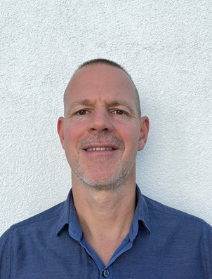 Mann mit kurzen Haaren und gestutztem Bart, der ein blaues Hemd trägt und vor einer weißen, strukturierten Wand steht. - © Keller / GB Kälte © Keller / GB Kälte